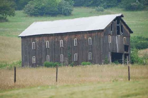 Two story brown wood barn with a gable roof and louvered side windows.