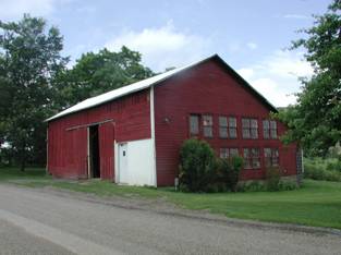 Large one story red wooden barn with sliding doors and rows of windows on the gable side